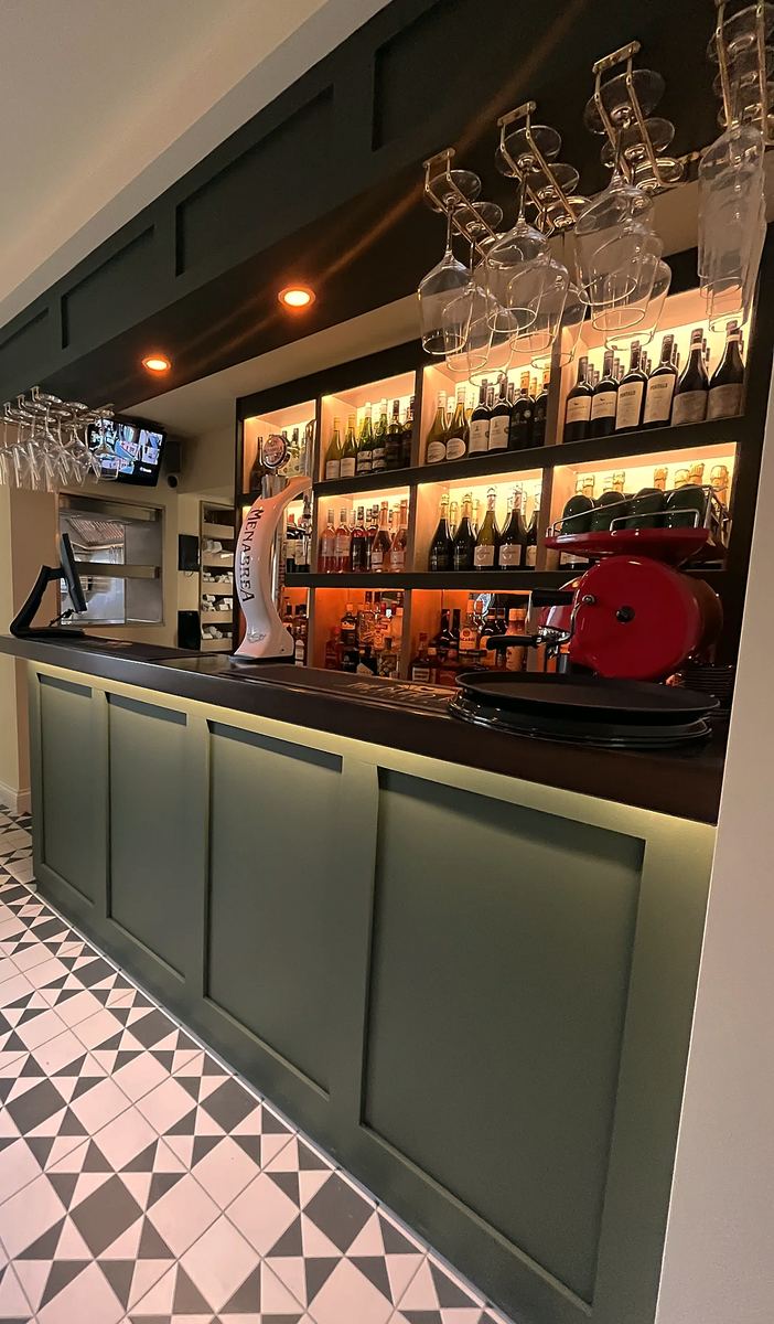 The bar inside, with dark green panelling, shelves of bottles and a black-and-white tiled floor