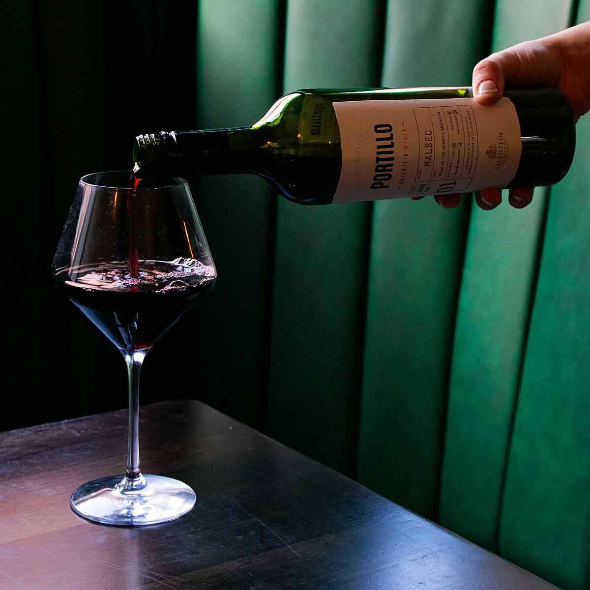 Red wine being poured into a glass in front of a green leather booth