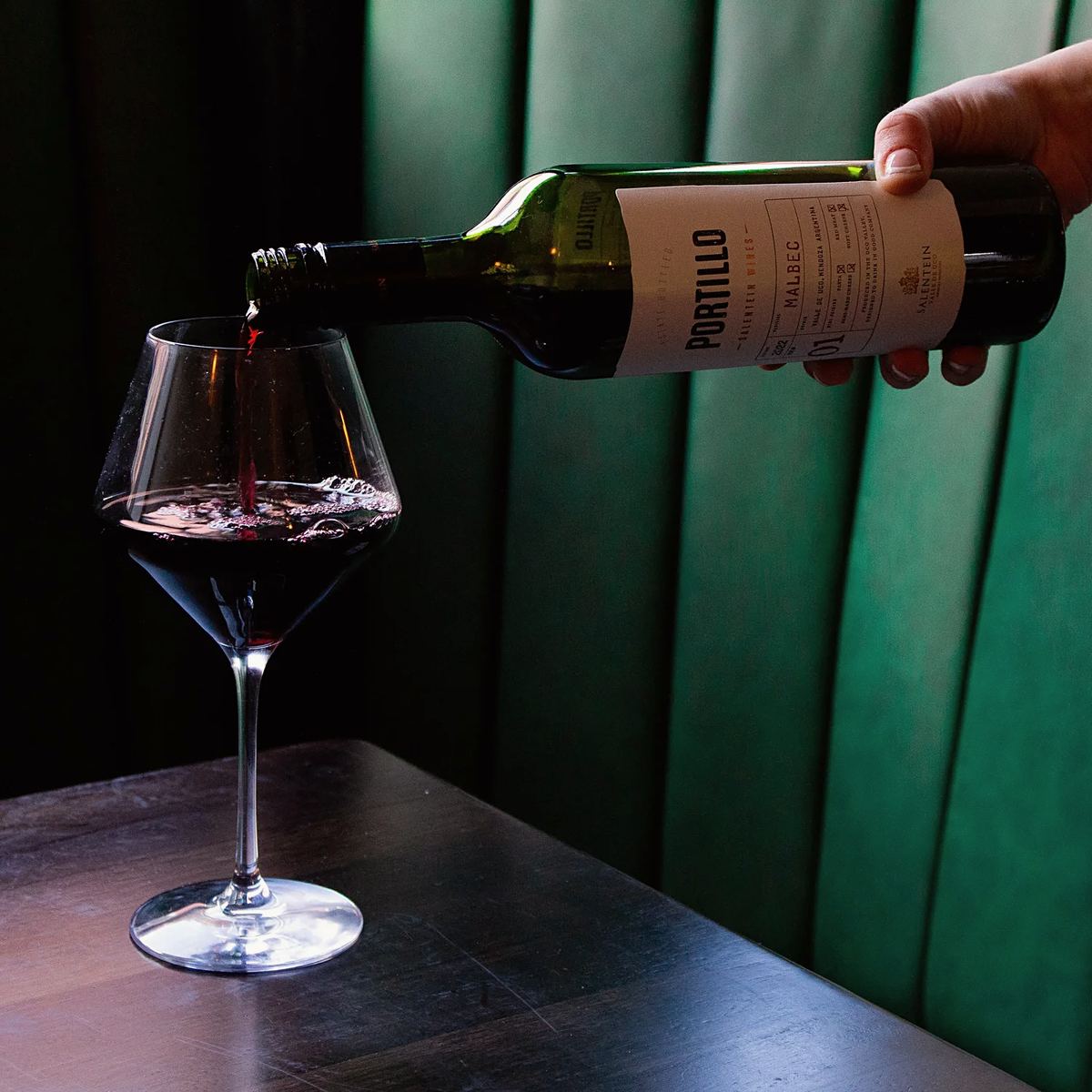 Red wine being poured into a glass in front of a green leather booth