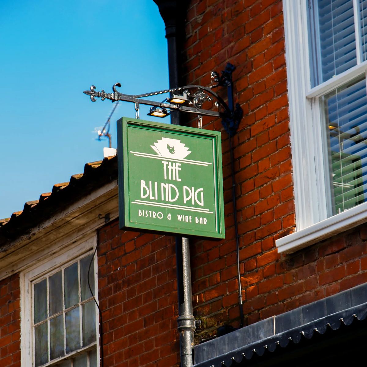 The green hanging sign, The Blind Pig, Bistro & Wine Bar, against red brick