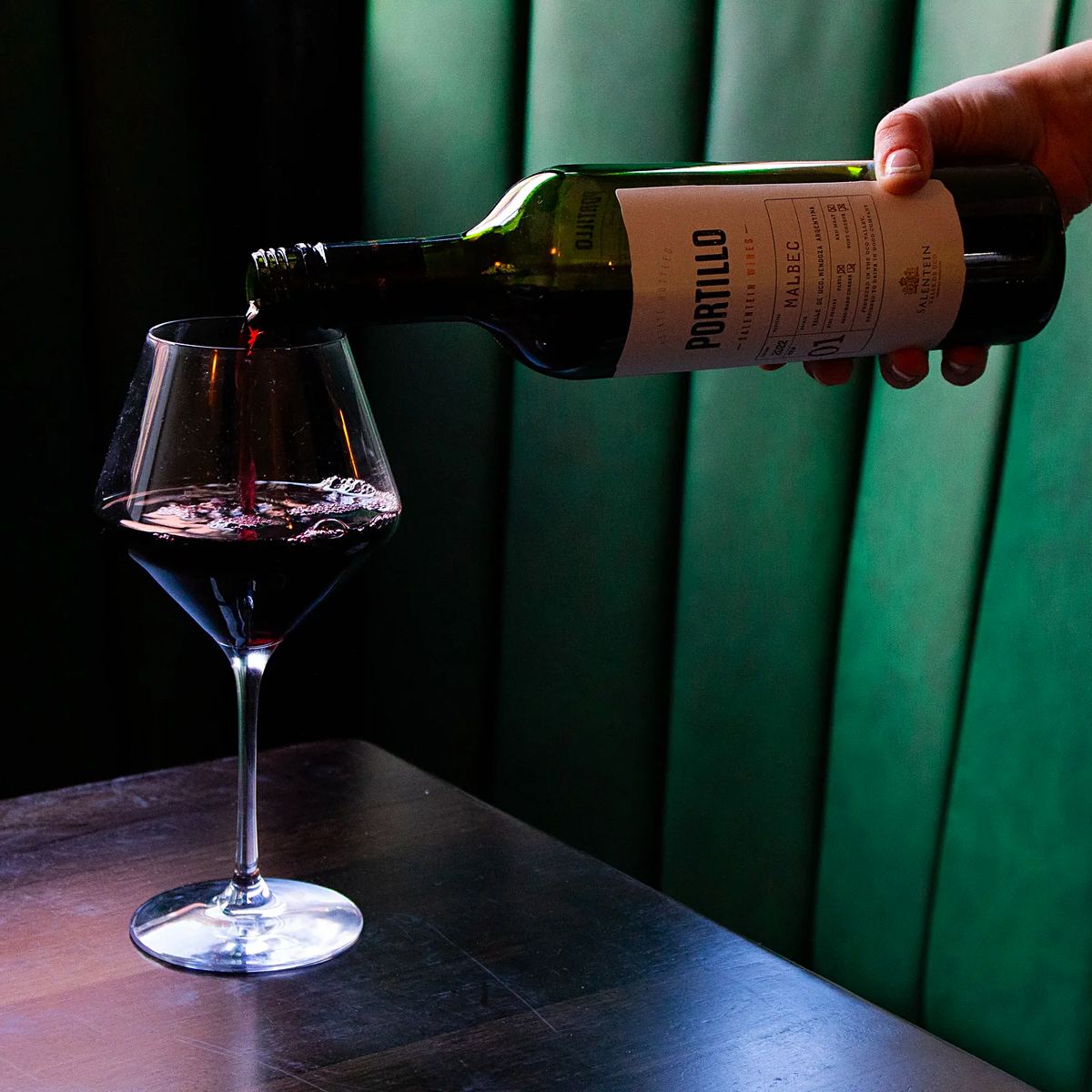 Red wine being poured into a glass in front of a green leather booth